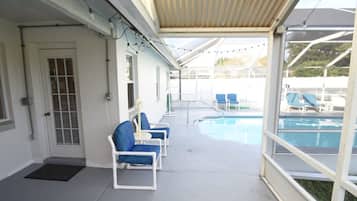 A covered outdoor area with a pool, blue lounge chairs, and a door with a window.