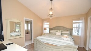 A bedroom with a large bed, a bedside table, a mirror, and a chandelier. - Perfect Paradise Vacation in Tranquility - Salt Water Pool (Palm Coast)