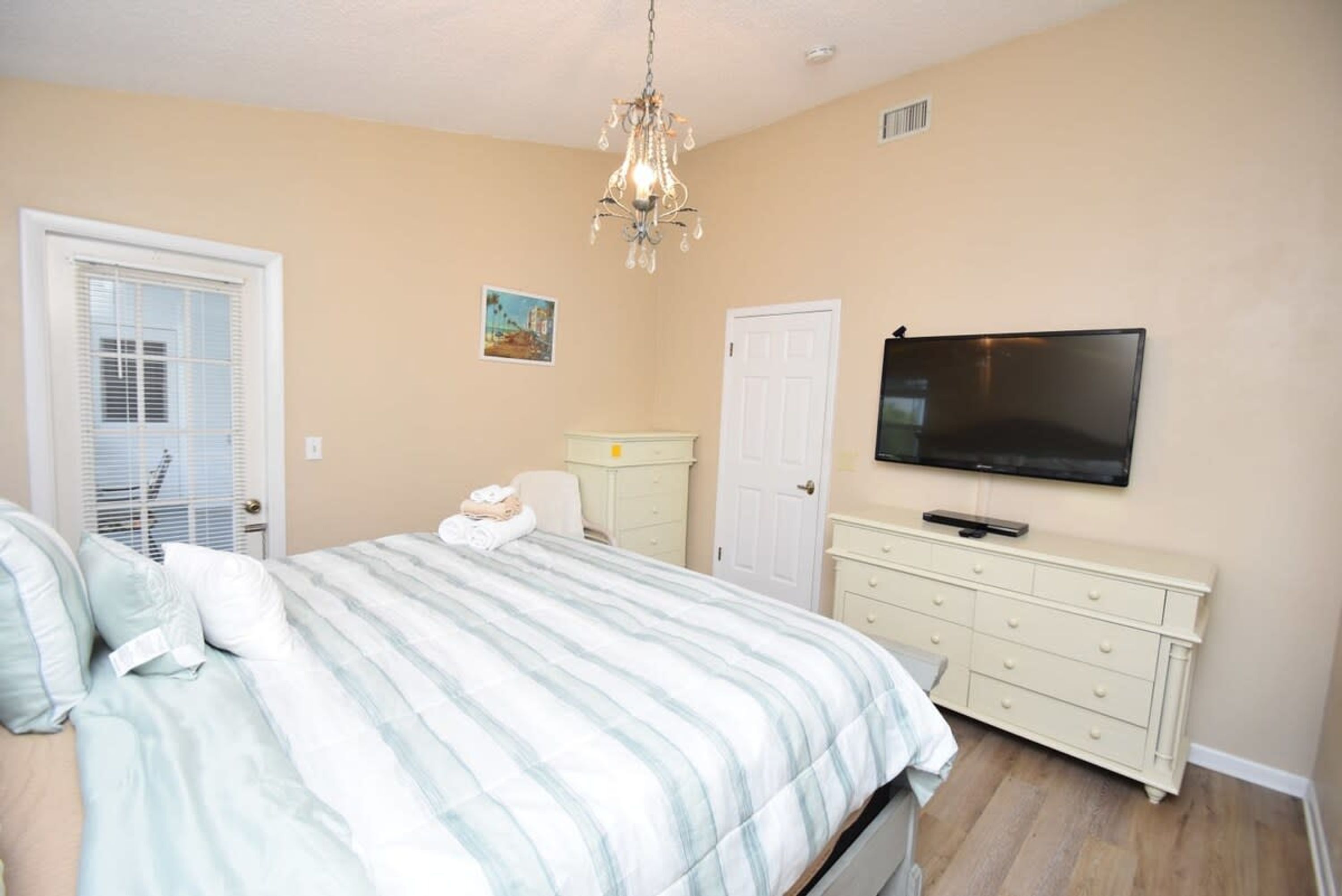 Une chambre à coucher avec un lit, une commode, un téléviseur, un lustre et une porte.