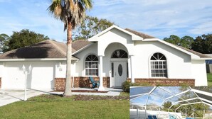 A two-story house with a covered swimming pool, a palm tree, and a brick foundation. - Perfect Paradise Vacation in Tranquility - Salt Water Pool (Palm Coast)