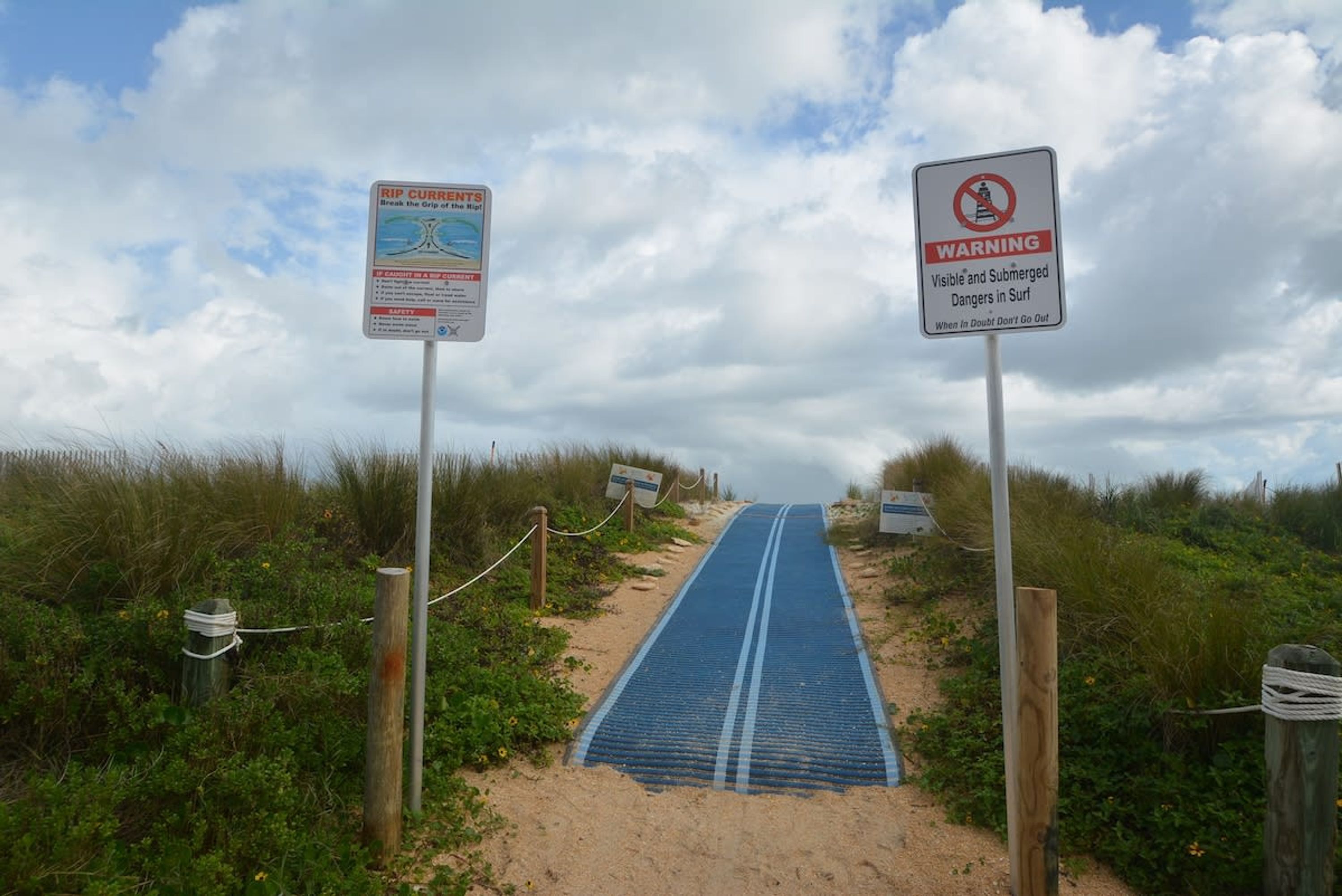 Een strandpad met waarschuwingsborden en een blauwe mat naar het water.