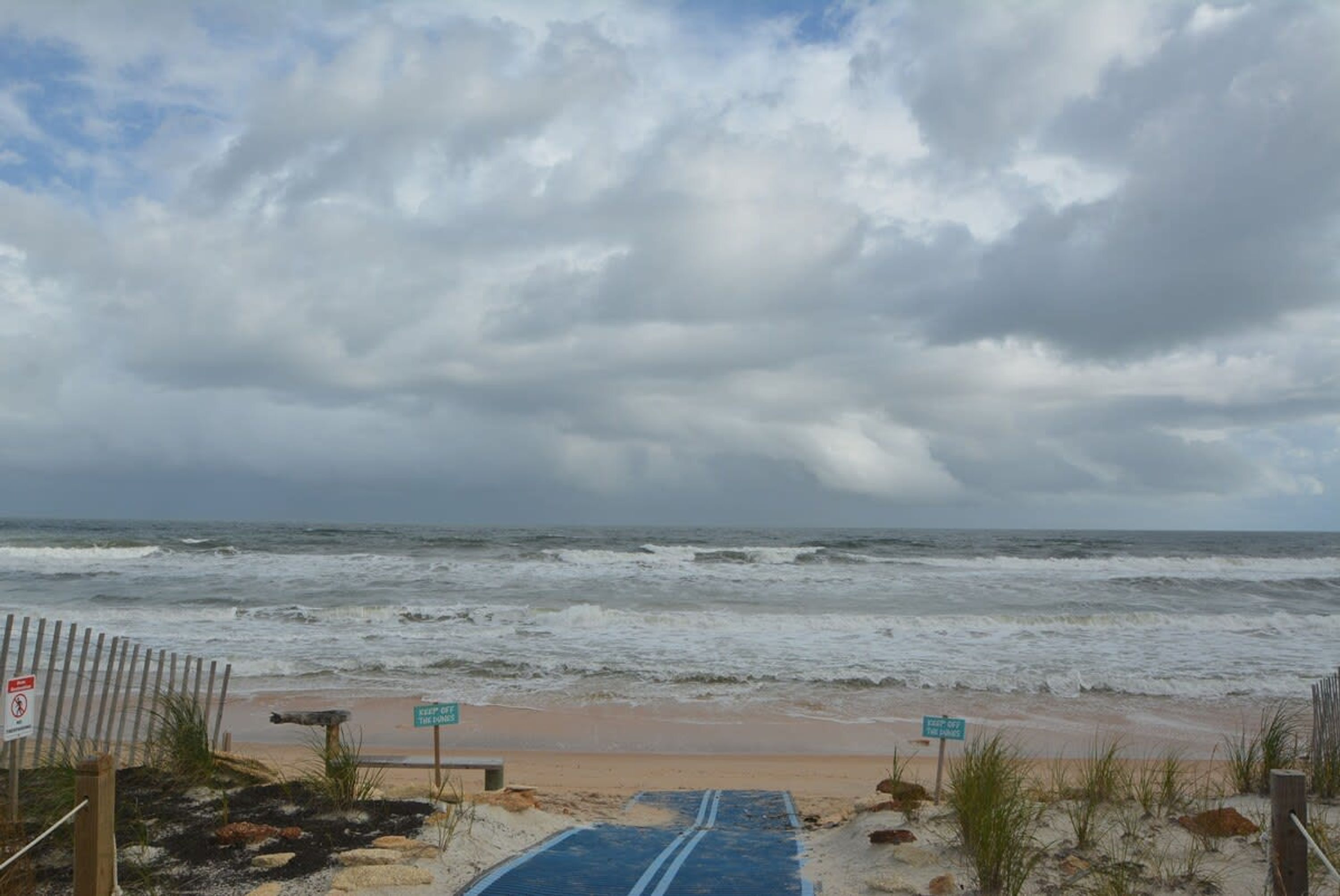 A beach with a wooden fence, a blue mat leading to the water, and signs indicating 'Keep Out' and 'No Swimming'.