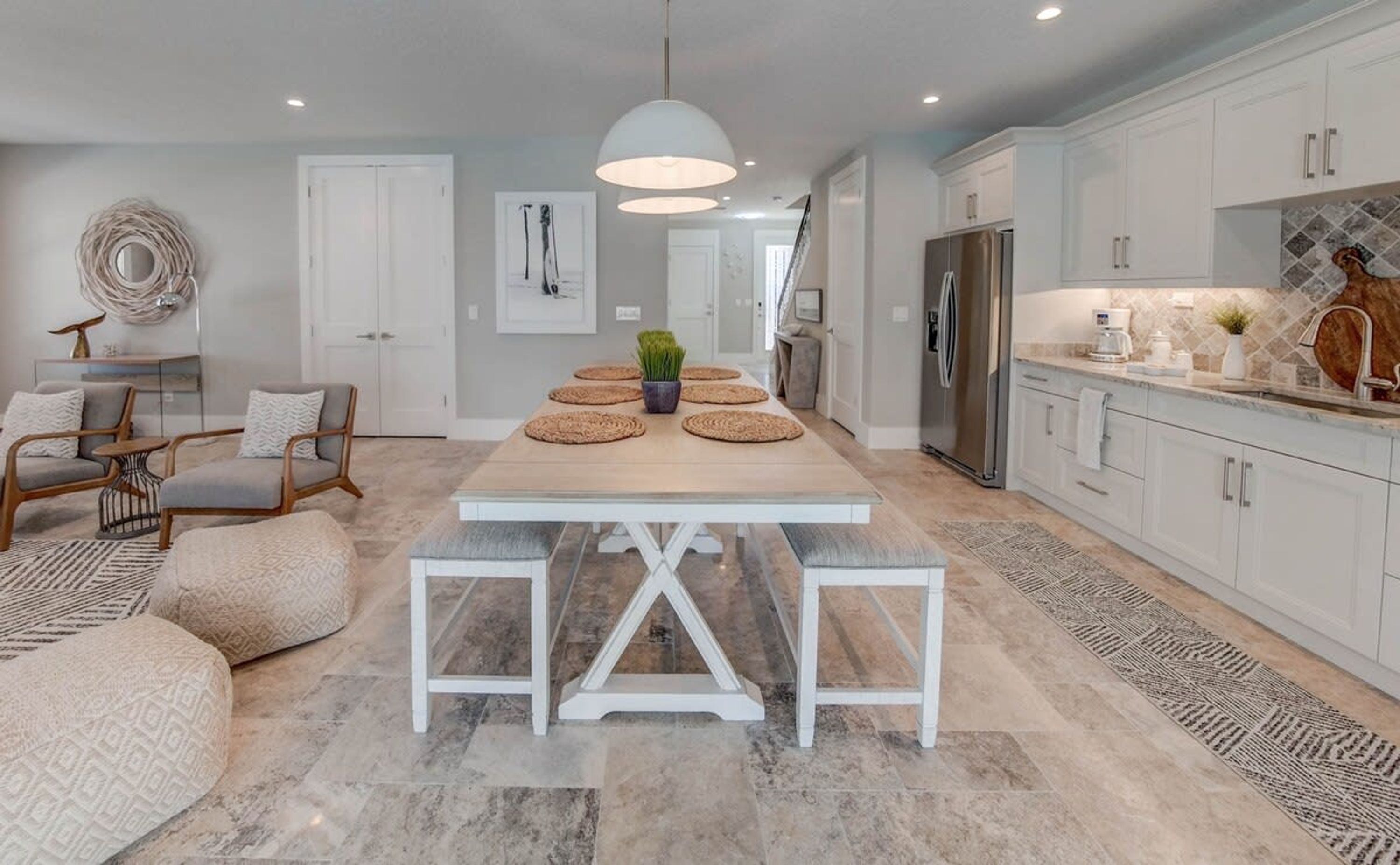 A modern kitchen with white cabinetry, a central island, and a dining area with a light-colored table and benches.