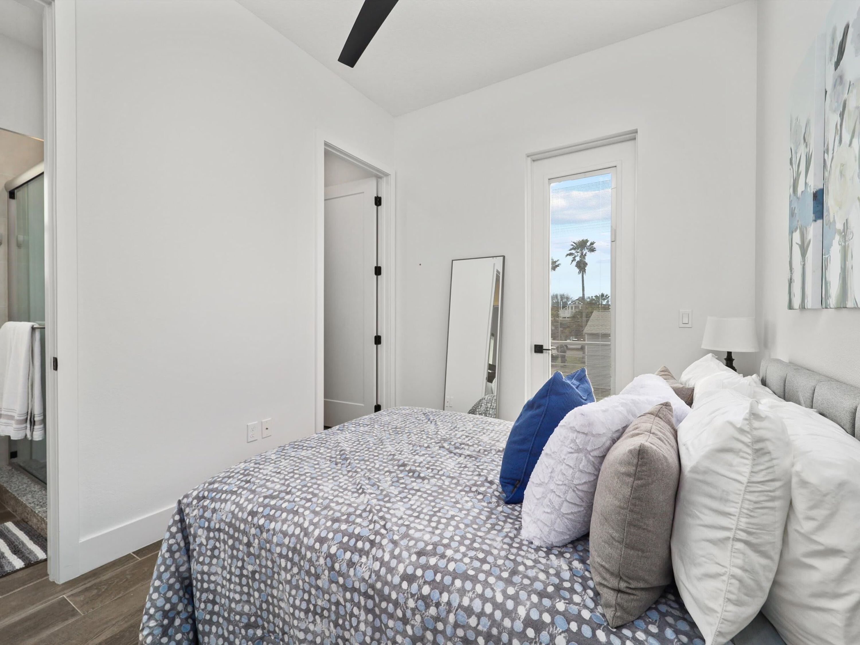 A bedroom with a bed, a door, a window, and a painting on the wall.