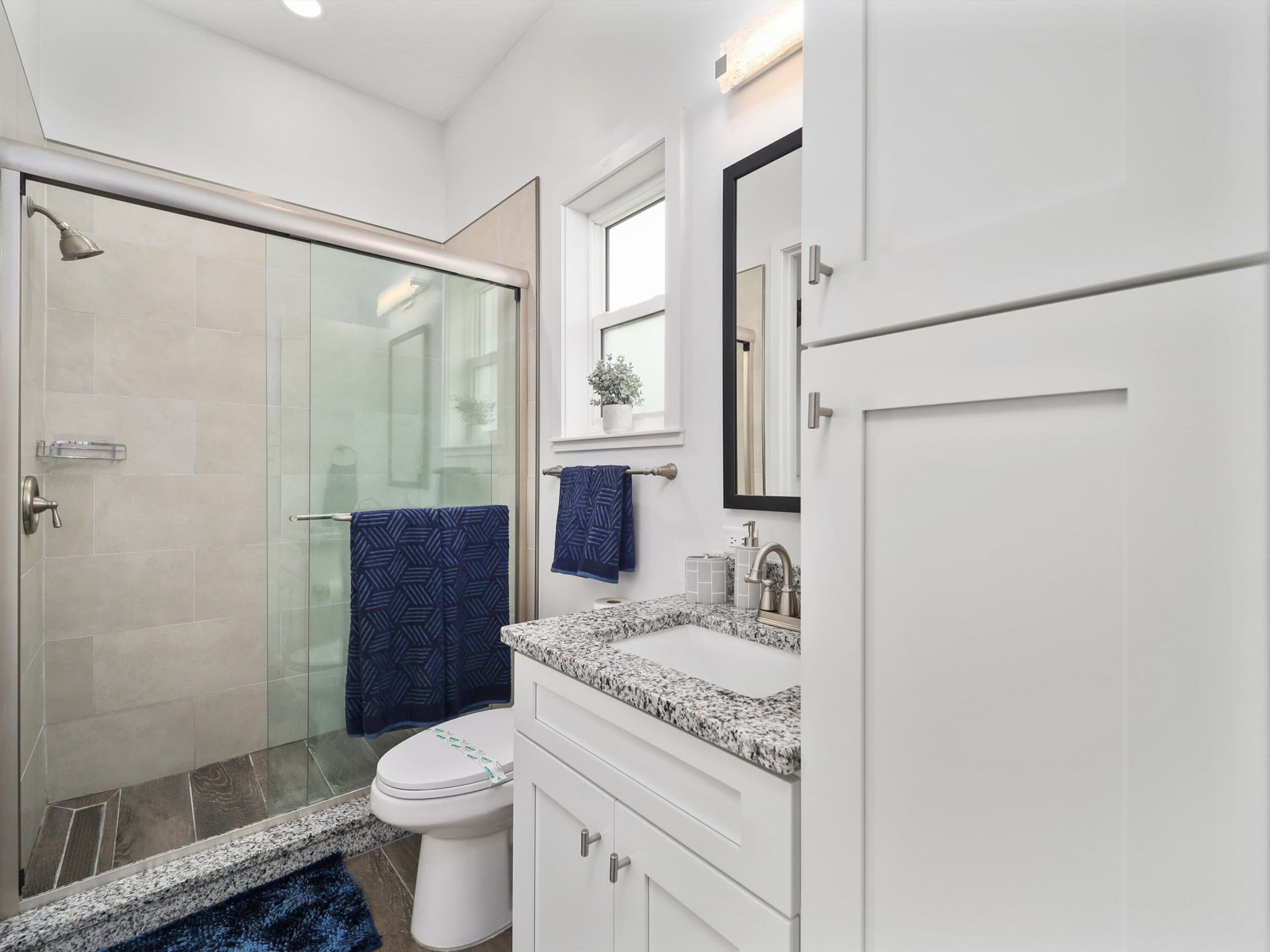 A modern bathroom with a glass shower enclosure, a white toilet, a granite countertop sink, and a large mirror.