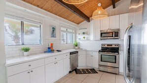 A modern kitchen with white cabinets, stainless steel appliances, and a wooden ceiling. - Pelican Beach Private Ocean Front Beach House- Sleeps 10 Bring Your Surf Boards (Palm Coast)