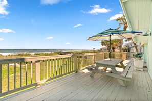A wooden deck with a picnic table and striped umbrella, overlooking a beach with a wooden railing. - Pelican Beach Private Ocean Front Beach House- Sleeps 10 Bring Your Surf Boards (Palm Coast)