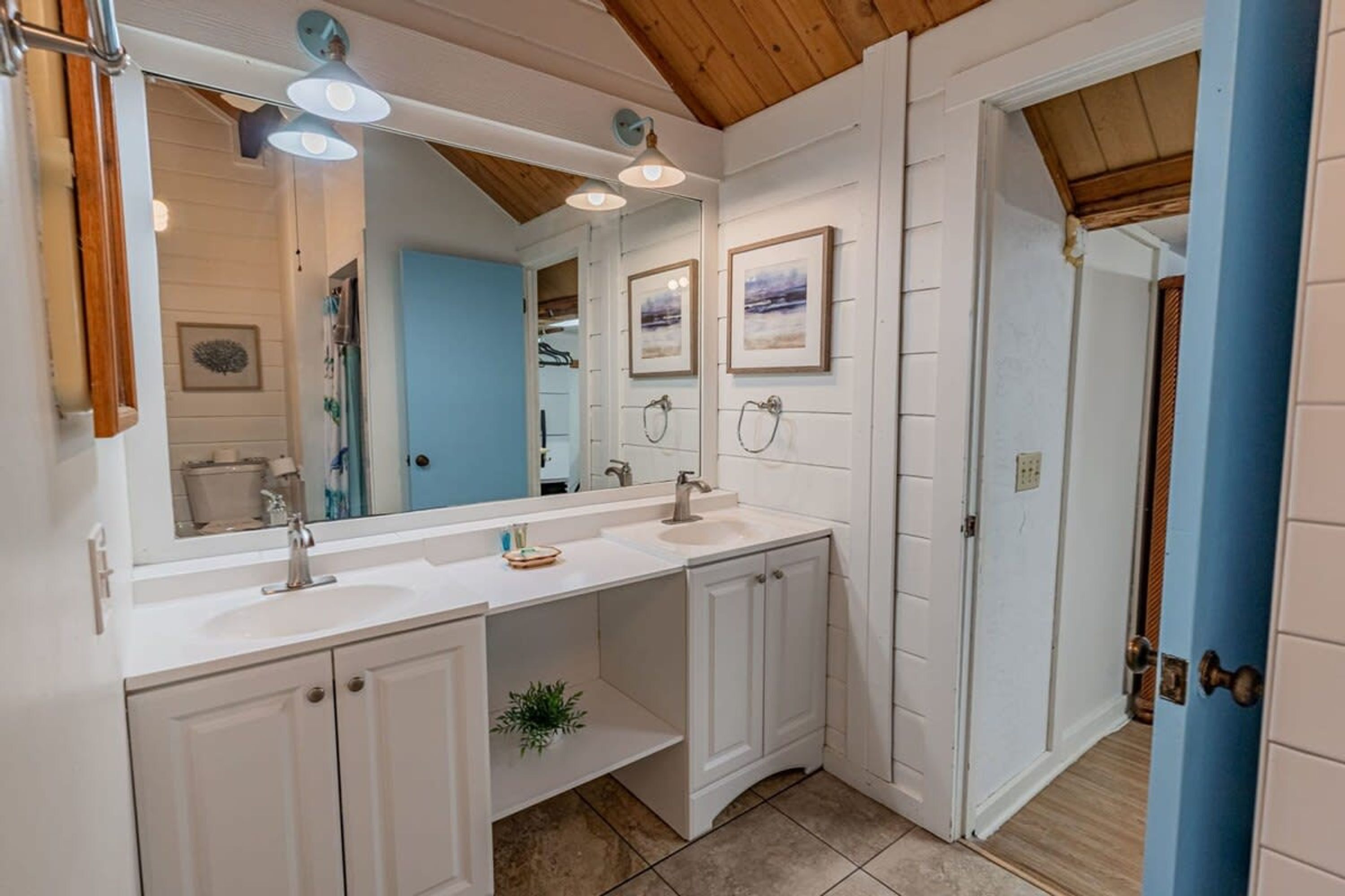 A bathroom with a white vanity, a large mirror, and framed artwork on the wall.