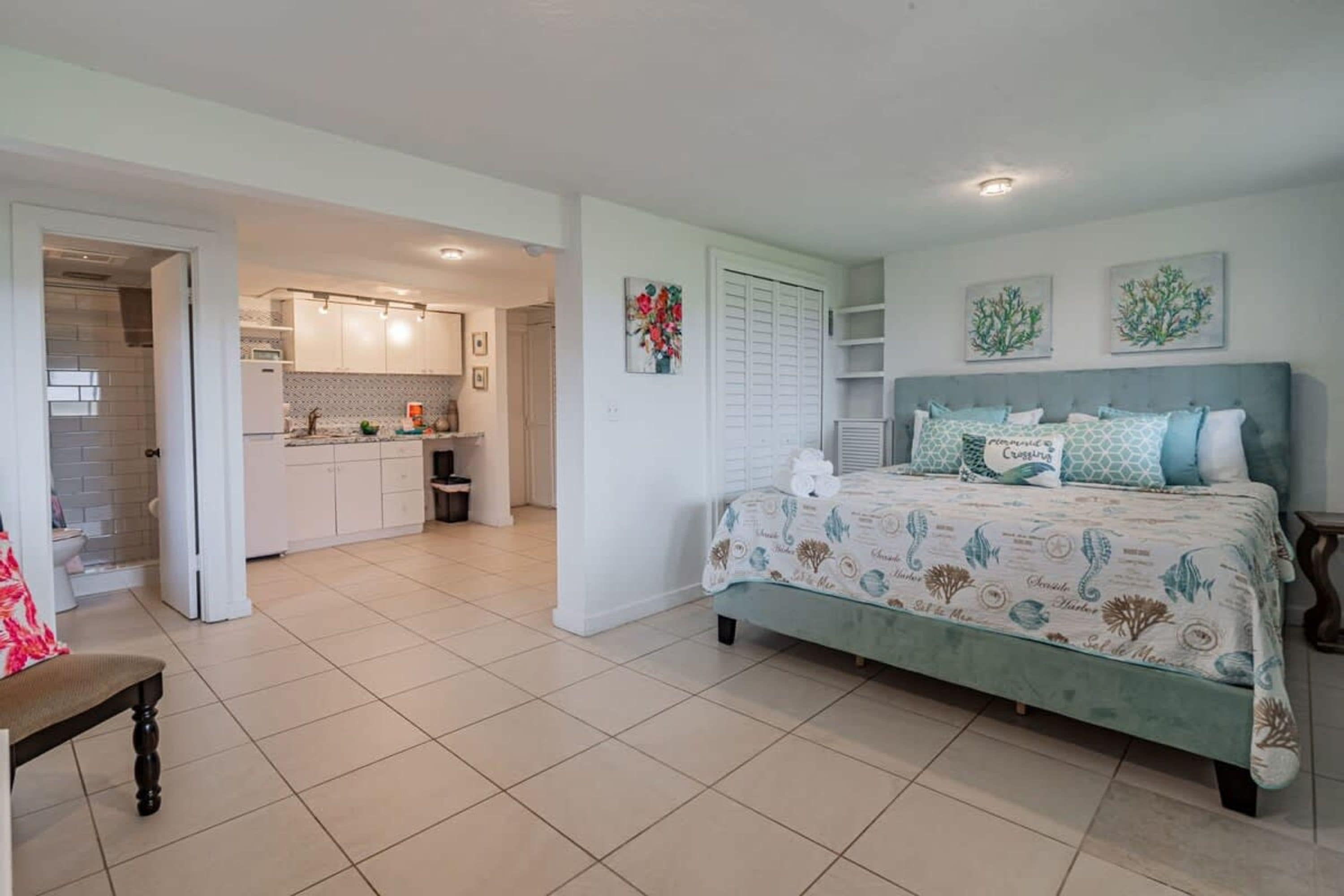 A bedroom with a bed, a chair, a bathroom, and a kitchen.