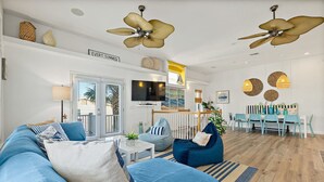 A modern living room with a blue sofa, a dining area with a white table, and a ceiling fan. - Perfect Beach House 2min Walk With Heated Pool and Hot Tub 4 bed 3 Bath With Pet Friendly (Palm Coast)