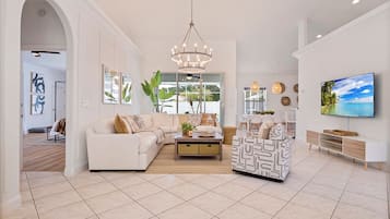 A spacious living room with a large sofa, a patterned armchair, and a television on the wall.