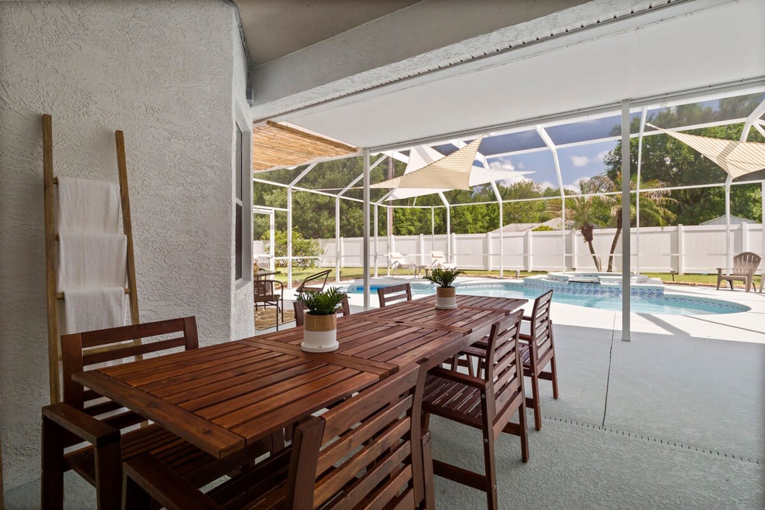 A covered patio area with a wooden table and chairs, a pool, and a view of the outdoors.