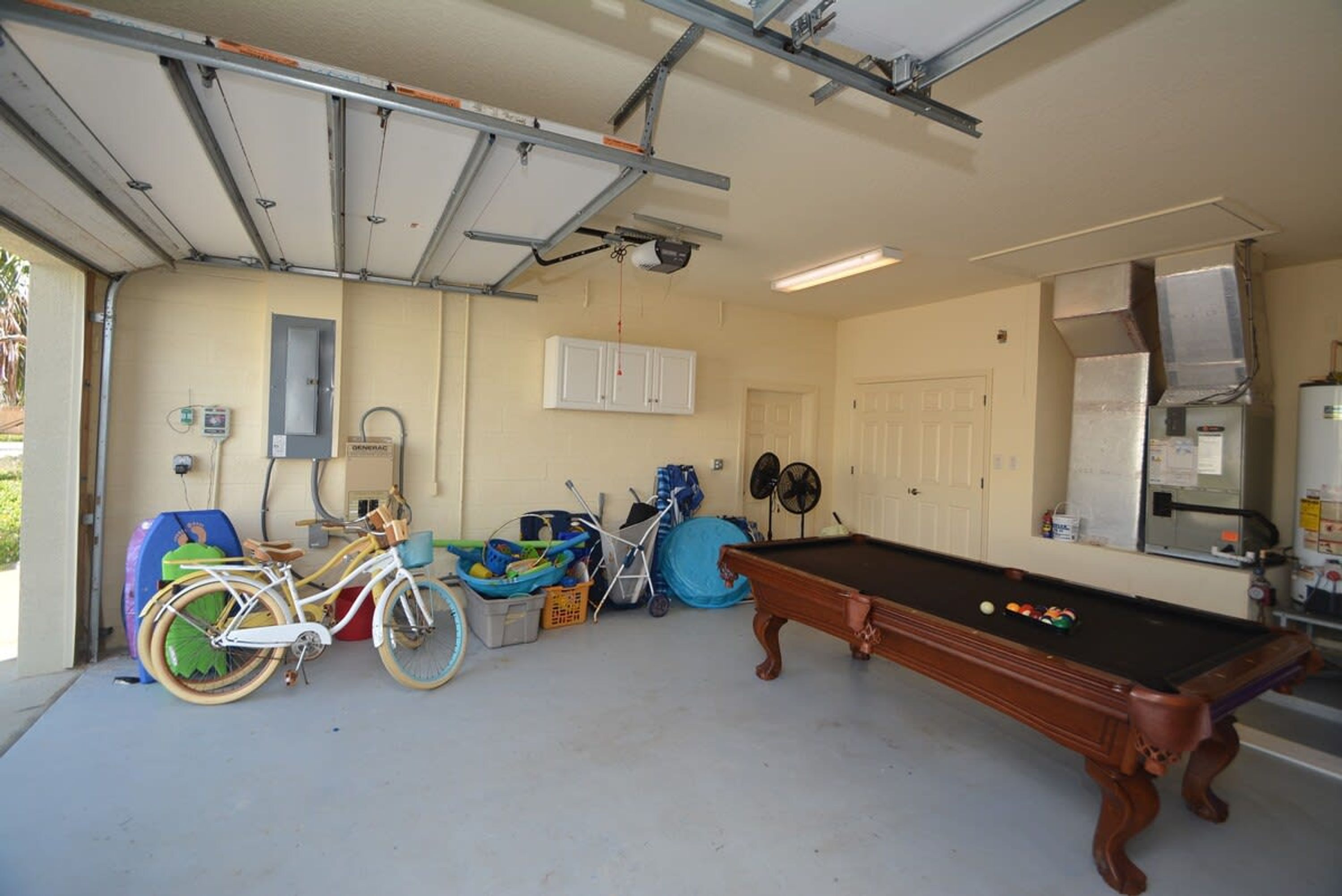 A garage with a pool table, bicycles, and a fan.