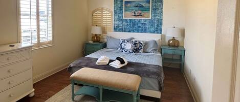 A bedroom with a bed, a bench, a dresser, a ceiling fan, and a window with blinds.