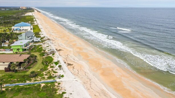 Una propiedad frente a la playa con una extensa playa arenosa, algunos edificios y una vista despejada del océano.