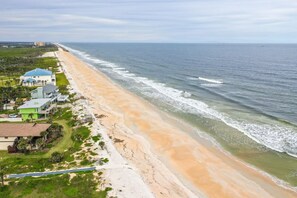 A beachfront property with a long sandy beach, a few buildings, and a clear view of the ocean.