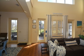 A living room with a sofa, a coffee table, and a dining area with a table and chairs. There are two doors leading to a patio.
