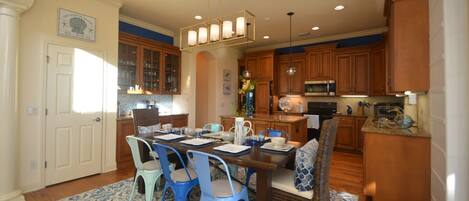 A spacious kitchen with wooden cabinets, a dining area with blue chairs, and a chandelier.