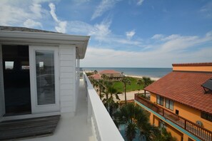 Varanda com vista para uma praia e oceano, com um edifício distante.