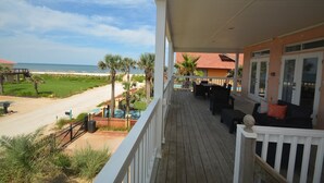 Eine Holzterrasse mit Gartenmöbeln, Blick auf den Strand und ein Poolbereich.