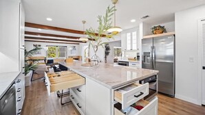 A modern kitchen with white cabinetry, a central island with drawers, pendant lighting, and a stainless steel refrigerator.