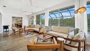 A spacious living room with a large window, a sofa set, wooden furniture, and a dining area.