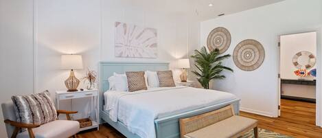 A bedroom with a bed, bedside tables, a chair, a bench, a ceiling fan, wall art, and a door with a fish decoration.