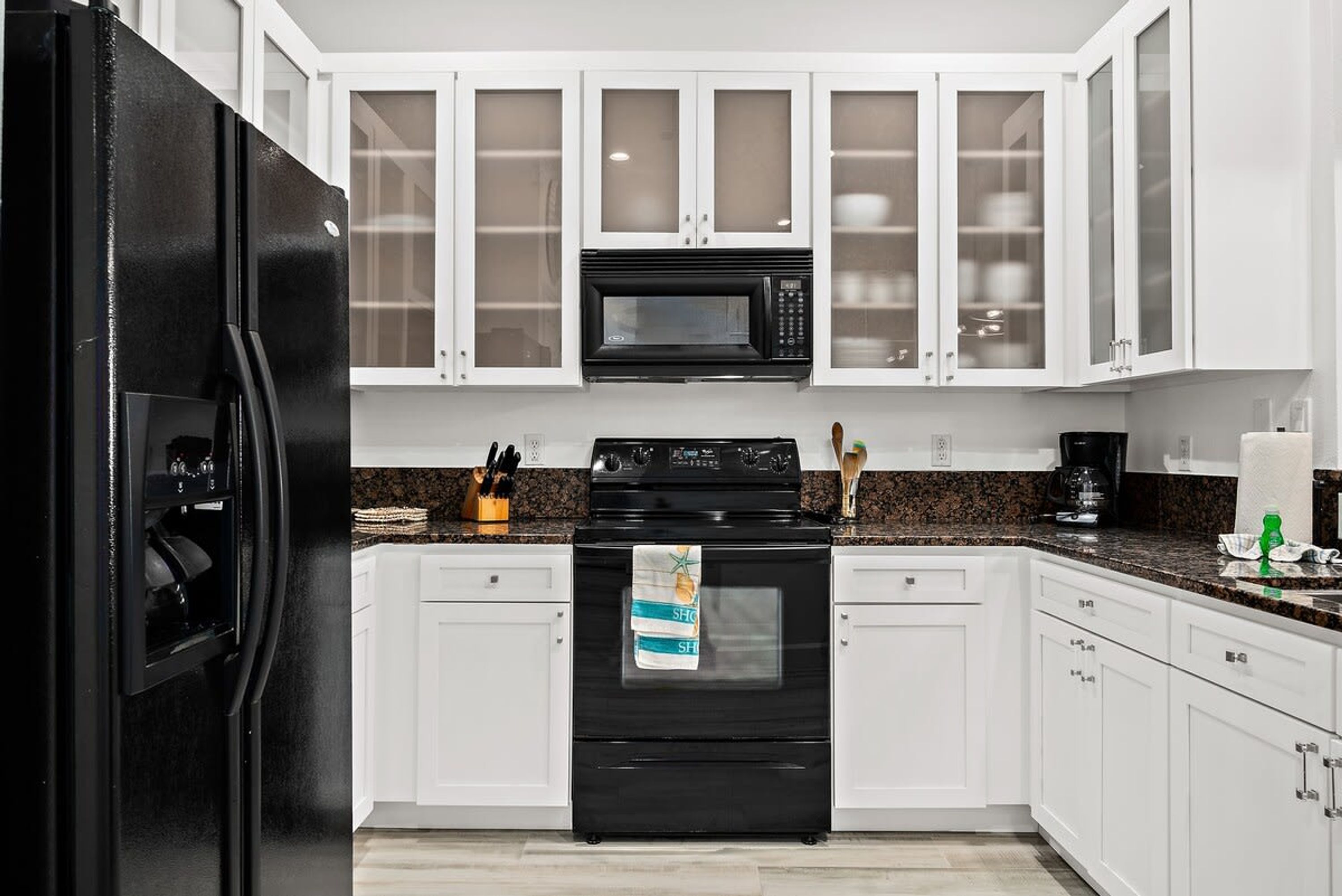 A kitchen with white cabinets, a black refrigerator, a microwave, and a stove.