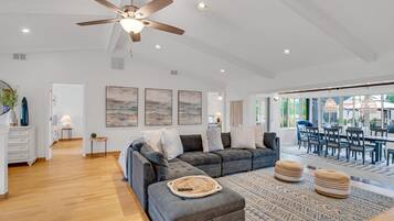 A spacious living room with a gray sectional sofa, a ceiling fan, and a dining area with a large table and chairs.