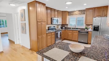A modern kitchen with wooden cabinets, granite countertops, stainless steel appliances, and a large island with a bowl.