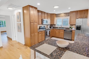 A modern kitchen with wooden cabinets, granite countertops, stainless steel appliances, and a large island with a bowl. - Saltwater Canal Home Heated Pool 3 2 2 Gorgeous Pets Welcome (Palm Coast)