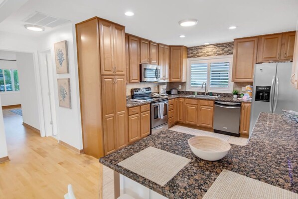A modern kitchen with wooden cabinets, granite countertops, stainless steel appliances, and a large island with a bowl. - Saltwater Canal Home Heated Pool 3 2 2 Gorgeous Pets Welcome (Palm Coast)