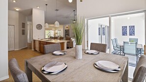 Un comedor con una mesa de madera dispuesta para cuatro personas, una planta en maceta y vistas de la cocina y la sala de estar.