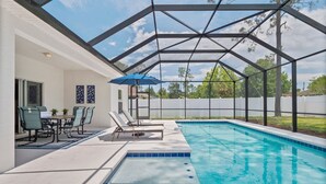 Una piscina exterior cubierta con sillas de descanso y una mesa, rodeada por una valla blanca y árboles.