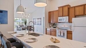 Una cocina moderna con armarios de madera, un refrigerador blanco, un microondas y un horno. Hay una isla grande con un lavamanos y un comedor con sillas y una mesa.