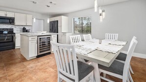 Una cocina moderna con muebles blancos, horno integrado y un comedor con mesa y sillas blancas.