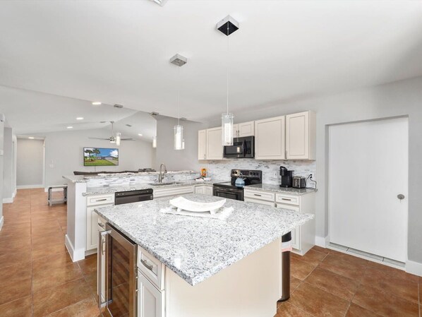 A modern kitchen with white cabinets, granite countertops, a central island, and a built-in microwave. - Waterside Pool Paradise (Palm Coast)