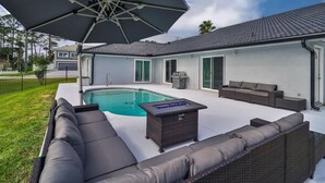 Un área de piscina moderna al aire libre con un jacuzzi integrado, una sombrilla grande y un espacio de descanso con sofá y mesa.