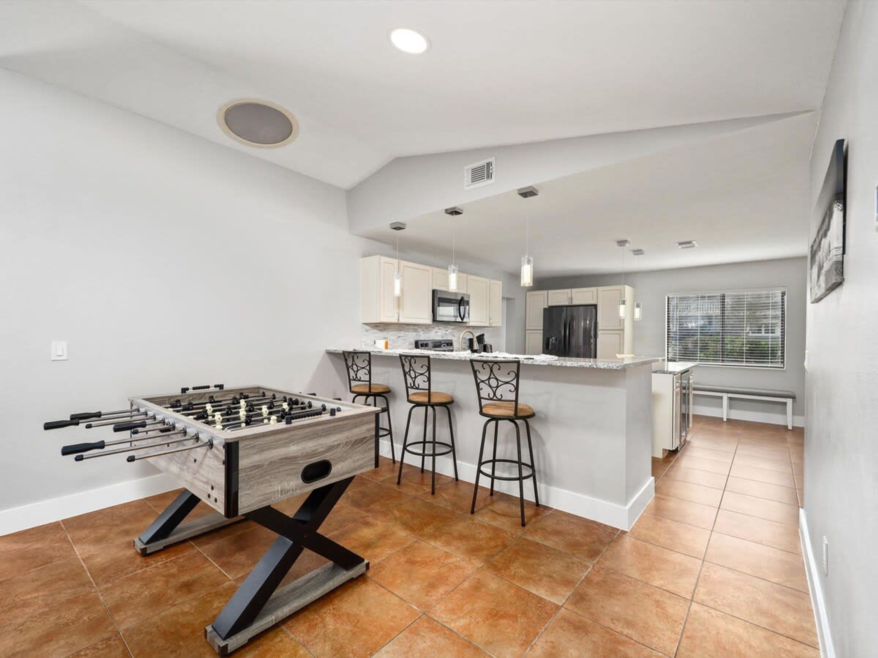 A modern kitchen with a foosball table, bar stools, and a central island with a sink and microwave.