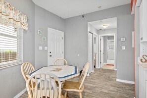 A dining area with a table and chairs, a window with blinds, and a door leading to another room.