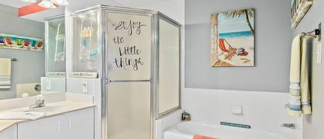 A modern bathroom with a glass shower enclosure, a bathtub, a vanity with a sink, and a towel rack.
