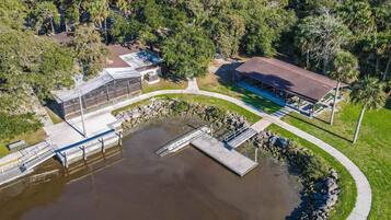 An aerial view of a lakeside property with a dock, a covered pavilion, and a building with a sloped roof.