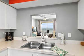 A modern kitchen with a double sink, a coffee maker, and a view of the balcony. - Oceanview Top-floor Penthouse in Surf Club Beach Pool Access (Palm Coast)