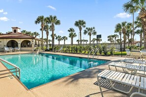 A swimming pool with lounge chairs, palm trees, and a building with arches. - Oceanview Top-floor Penthouse in Surf Club Beach Pool Access (Palm Coast)