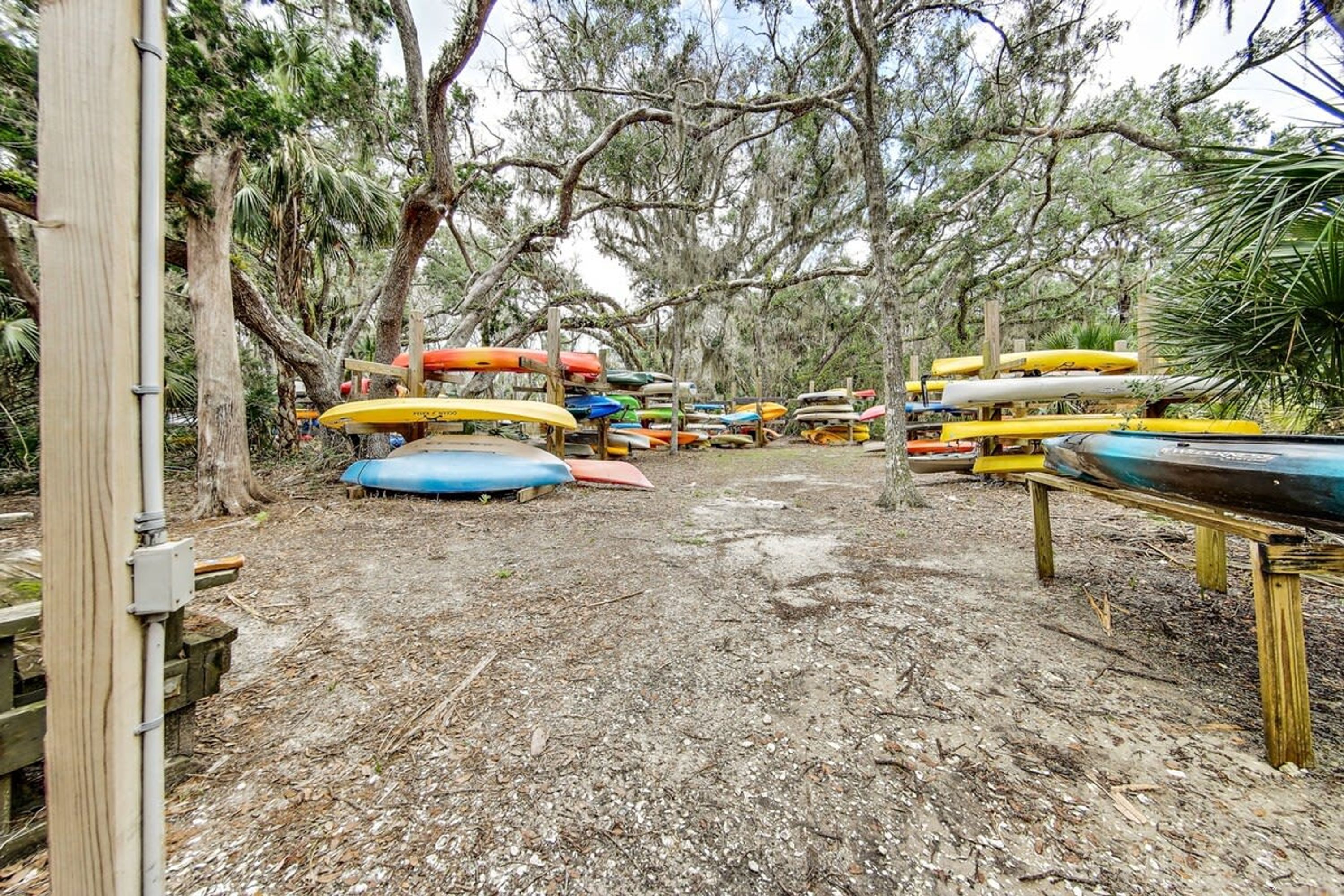 A collection of kayaks and canoes on wooden stands in a wooded area.