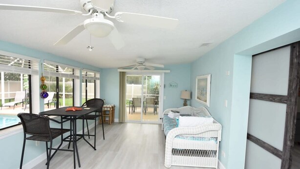 A room with a dining table, chairs, a white wicker sofa, a ceiling fan, and a view of the outside. - Hidden Oasis Spacious Home With Salt Water Heated Pool Hot Tub Fenced Yard Pets are Welcome (Palm Coast)
