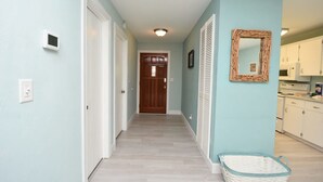 A hallway with light blue walls, a wooden door at the end, and a basket on the floor. - Hidden Oasis Spacious Home With Salt Water Heated Pool Hot Tub Fenced Yard Pets are Welcome (Palm Coast)