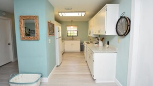 A narrow hallway with light blue walls, a white door, a wicker mirror, and a basket on the floor. - Hidden Oasis Spacious Home With Salt Water Heated Pool Hot Tub Fenced Yard Pets are Welcome (Palm Coast)