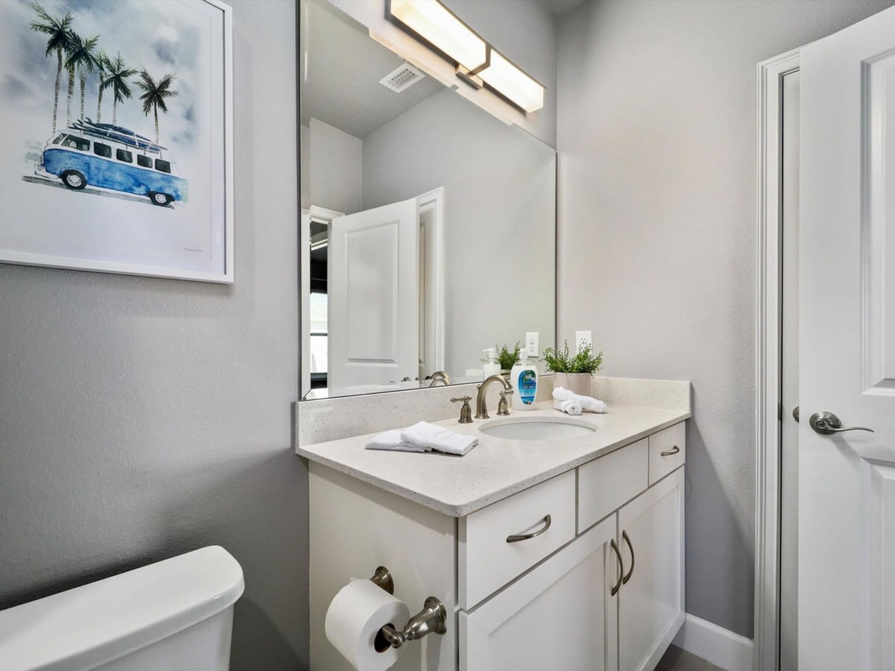 Un baño con inodoro blanco, lavamanos con espejo y un perchero para toallas.