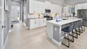 A modern kitchen with white cabinetry, a central island with bar stools, stainless steel appliances, and recessed lighting. - Seabliss Steps to the Beach Pool Home 4 4 5 new (Palm Coast)